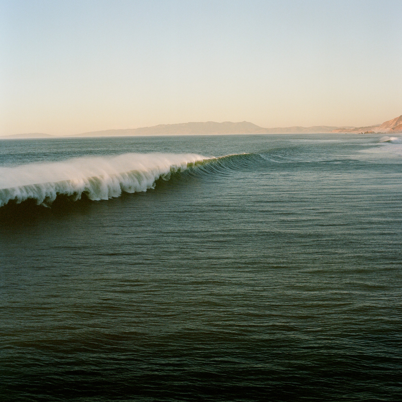 Wave crashing in the ocean with a mountainous landscape in the background
